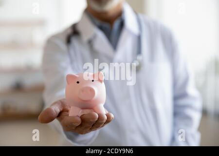 Primo piano medico maturo che indossa uniforme tenendo rosa piggy bank Foto Stock