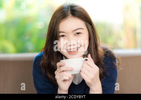 Belle donne asiatiche che bevono caffè caldo seduto sul divano vintage in caffetteria Foto Stock