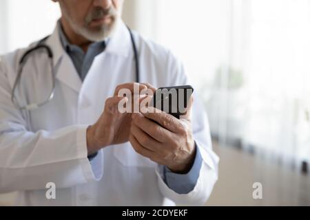 Primo piano medico senior tramite telefono, app di telemedicina, lavoro online Foto Stock