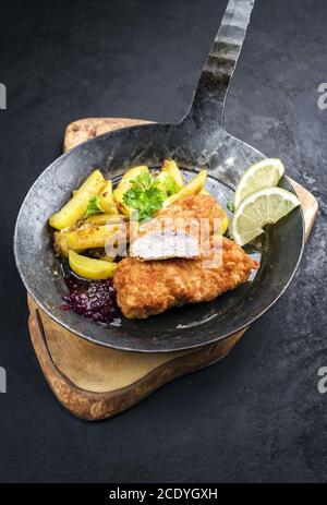Tradizionale bistecca di vitello fritta con patate arrosto e mirtillo rosso salsa offerta come closeup in un rustico ferro battuto vecchio skille Foto Stock