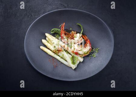 Tradizionale barbecue coda di aragosta speziata tagliata a fette e offerto con bianco asparagi e lattuga come vista dall'alto su un design moderno piastra Foto Stock