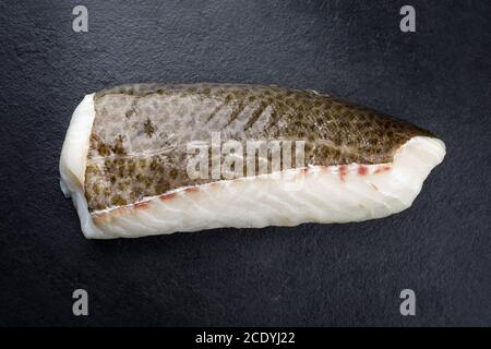 Filetto crudo di merluzzo norvegese skrei con la pelle come closeup su lavagna nera con spazio per la copia Foto Stock