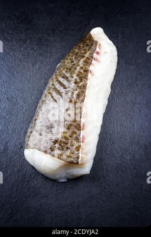 Filetto crudo di merluzzo norvegese skrei con la pelle come closeup su lavagna nera con spazio per la copia Foto Stock