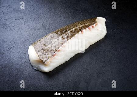 Filetto crudo di merluzzo norvegese skrei con la pelle come closeup su lavagna nera con spazio per la copia Foto Stock