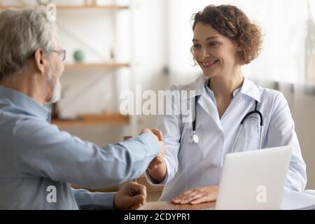 Sorridente giovane medico scuotendo la mano paziente matura alla riunione Foto Stock