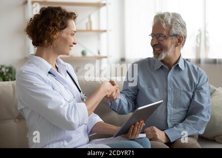 Sorridente paziente maturo scuotendo la mano dell'infermiere del medico durante la riunione Foto Stock