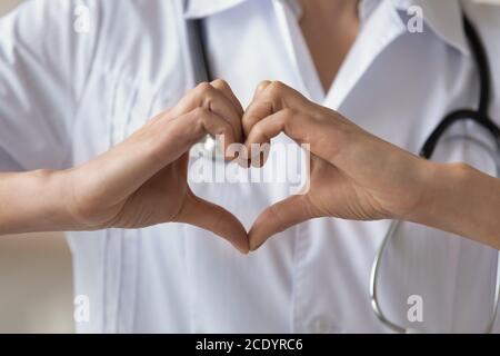 Primo piano giovane donna che indossa un medico uniforme che mostra il gesto del cuore Foto Stock