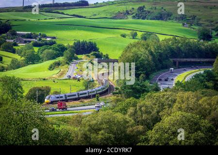 Un trenino Avantini Pendolino che si affaccia sulle curve della linea principale della Costa Ovest a Beck Foot vicino a Tebay, con la M6 che corre a fianco. Foto Stock