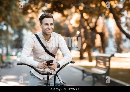 Stile Street. Uomo giovane ed elegante che sta testando al telefono mentre si siede in bicicletta Foto Stock