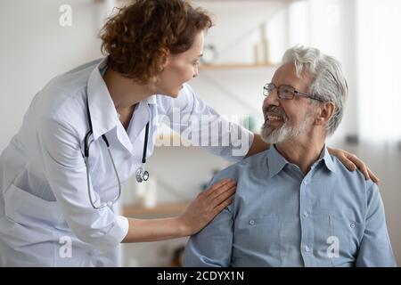 Giovane infermiera sorridente che assiste il paziente maturo durante la visita domicecare Foto Stock