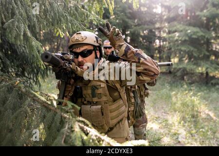 Ufficiale bearded in casco e occhiali da sole che contano giù prima dell'attacco mentre conducendo operazione militare in foresta Foto Stock