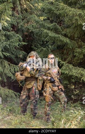 Ritratto di giovani soldati seri in abiti camouflage in piedi con arma contro alberi di foresta Foto Stock