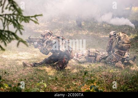 Il soldato dell'esercito spara a fucile mentre copre i colleghi sul campo di battaglia fumoso Foto Stock
