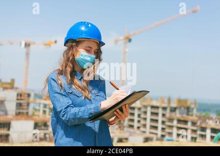 giovane donna ingegnere indossare maschera viso durante il lavoro in costruzione sito Foto Stock