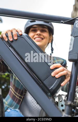 giovane donna che tiene una batteria per bicicletta elettrica montata sul telaio Foto Stock