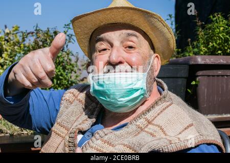 uomo anziano che indossa la maschera facciale mostrando pollici in alto segno Foto Stock