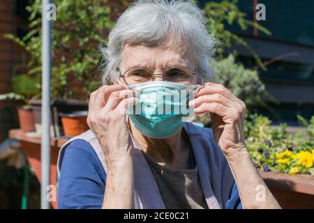 donna anziana che si mette su una maschera facciale Foto Stock