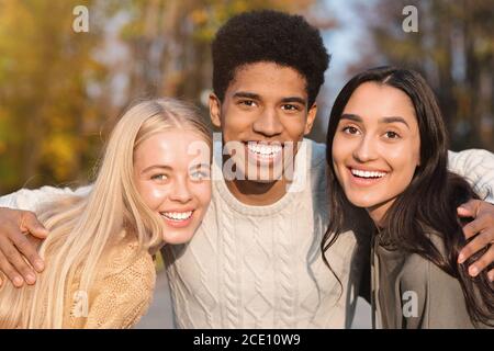 Ritratto di tre amici multietnici che sorridono sullo sfondo del parco Foto Stock