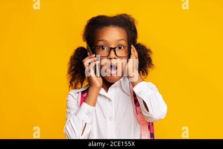 Shocked ragazza della scuola che parla al telefono con la bocca aperta, studio Foto Stock