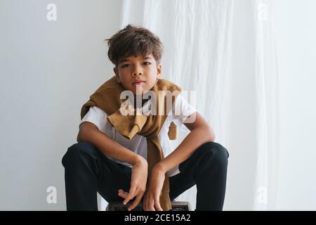 Un bambino indiano asiatico senza emozioni che guarda la telecamera, seduto in basso, si inginocchia Foto Stock