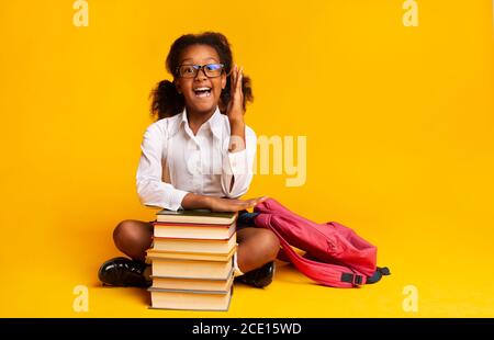 Nerdy Schoolgirl alzando la mano seduta a Libri su sfondo giallo Foto Stock