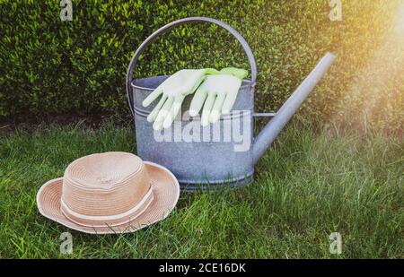 Annaffiatoio, guanti da giardino e cappello estivo su erba verde Foto Stock