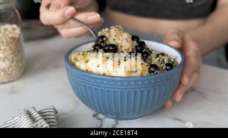 Donna fitness che mangia porridge di farinata d'avena vegana con banana, semi di canapa e bacche per una colazione sana. Alimentazione sostenibile, concetto di stile di vita sano Foto Stock