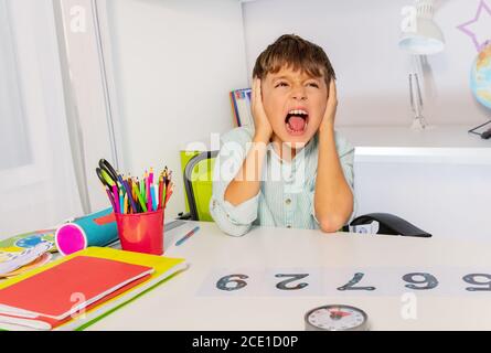 Ragazzo con autismo disordine spettro imparare i numeri, ma urlare e orecchie vicine nella classe, questione sensoriale Foto Stock