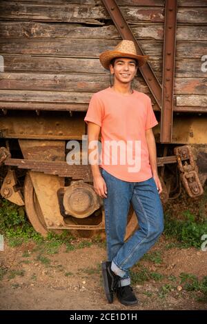 Young Man sorridente e in posa davanti a un vagone in legno vecchio treno. Ranch Concept Photography Foto Stock