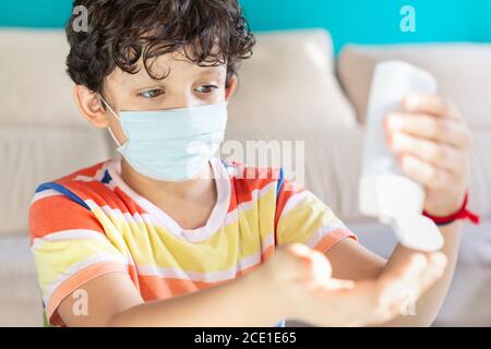 Bambino con una maschera per il viso che applica gel idroalcolico Le sue mani come misura preventiva durante la pandemia di Covid-19 Foto Stock