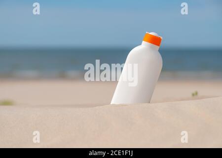 Crema di protezione solare nella sabbia in una giornata di sole in spiaggia. Bottiglia bianca crema solare protezione da scottature. Nessuno. Foto Stock