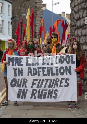 Caernarfon Castle, Galles, Regno Unito. 30 agosto 2020, i manifestanti della ribellione estinzione e la Brigata rossa ribelle prendono il controllo del Castello di Caernarfon per protestare sui cambiamenti climatici e sul riscaldamento globale. Le scarpe dei bambini significano che sono i bambini che soffriranno in futuro. I manifestanti hanno un banner che afferma il nostro futuro in rovine con bandiere rosse, arancioni e gialle Credit: Denise Laura Baker/Alamy Live News Foto Stock