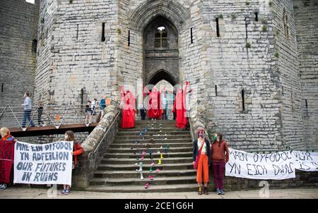 Caernarfon Castle, Galles, Regno Unito. 30 agosto 2020, i manifestanti della ribellione estinzione e la Brigata rossa ribelle prendono il controllo del Castello di Caernarfon per protestare sui cambiamenti climatici e sul riscaldamento globale. Le scarpe dei bambini significano che sono i bambini che soffriranno in futuro. I ribelli rossi posano sui gradini del castello di Caernarfon affiancati da striscioni in gallese Credit: Denise Laura Baker/Alamy Live News Foto Stock