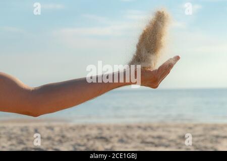 Primo piano di sabbia che si riversano dalla mano sulla spiaggia in una soleggiata giornata estiva. Giocare con la sabbia in vacanza. Foto Stock