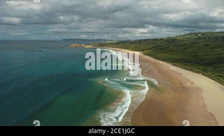 Irlanda vista aerea: spiaggia oceano baia acqua crashing. Le persone sulla riva camminano e giocano con i cani. Prati all'orizzonte. Pittoresca bellezza del Nord Foto Stock