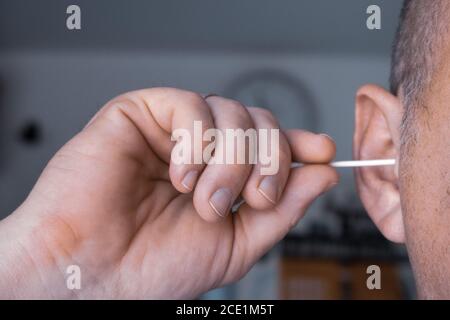 un uomo pulisce le orecchie con un bastoncino di cotone Foto Stock