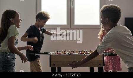 Gruppo di bambini carino multiculturale stand al coperto trascorrere il tempo di gioco con gli amici giocare a foosball insieme. Versione da tavolo degli amanti del calcio. Foto Stock