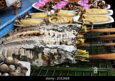 Primo piano di una distesa di pesce su una griglia all'aperto che propone delicatezze tailandesi di calamari e altro pesce al mercato galleggiante di Ayothaya, in Thailandia Foto Stock