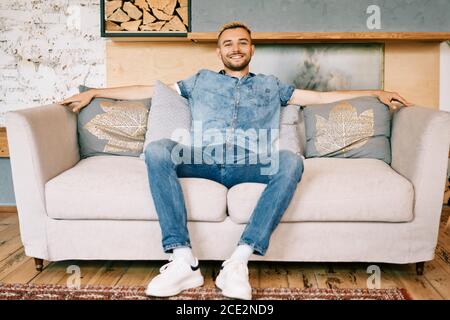 Bell'uomo sorridente rilassarsi sul divano a casa Foto Stock