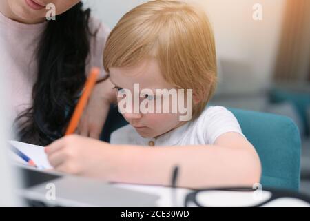 Madre che aiuta suo figlio a studiare le classi in linea a casa. COVID-19 tempi pandemici. Foto Stock