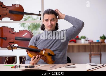 Giovane uomo riparatore che ripara il violino in officina Foto Stock