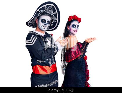 Giovane coppia che indossa il giorno messicano del costume morto sullo sfondo puntando da parte con le mani aperte palme mostrando spazio di copia, presentando la pubblicità Foto Stock