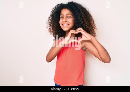 Bambino afroamericano con capelli ricci indossando abiti casual sorridente in amore facendo il simbolo del cuore forma con le mani. Concetto romantico. Foto Stock