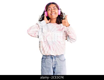 Giovane bella razza mista donna ascolto di musica con cuffie sorridenti felice e positivo, pollice su facendo eccellente e segno di approvazione Foto Stock