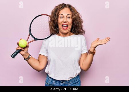 Giovane età bella sportivo che gioca a tennis tenendo racchetta e palla sfondo bianco che celebra il successo con sorriso felice e vincitore espr Foto Stock