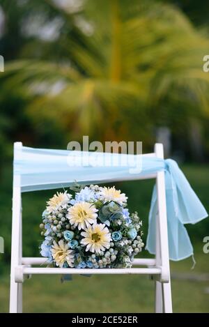 Primo piano di un mazzo di sposa seduto su una sedia bianca durante un matrimonio. Fiori bianchi e blu chiaro Foto Stock