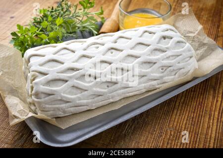 Carne di maiale cruda Kasseler come pezzo in pasta sfoglia e. tuorli d'uovo come closeup offerto su un tagliere di legno con erbe Foto Stock