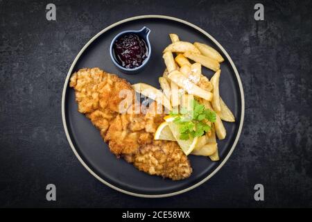 Wiener schnitzel fritto dalla parte superiore di vitello con patatine fritte e. salsa al mirtillo rosso come vista dall'alto su un piatto dal design moderno con copia sp Foto Stock