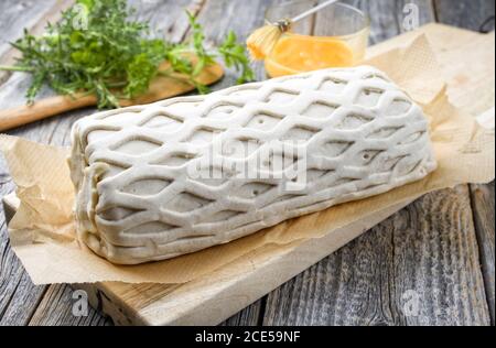 Carne di maiale cruda Kasseler come pezzo in pasta sfoglia e. tuorli d'uovo come closeup offerto su un tagliere di legno con erbe Foto Stock
