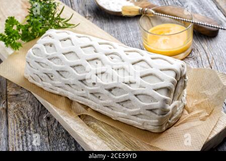 Carne di maiale cruda Kasseler come pezzo in pasta sfoglia e. tuorli d'uovo come closeup offerto su un tagliere di legno con erbe Foto Stock